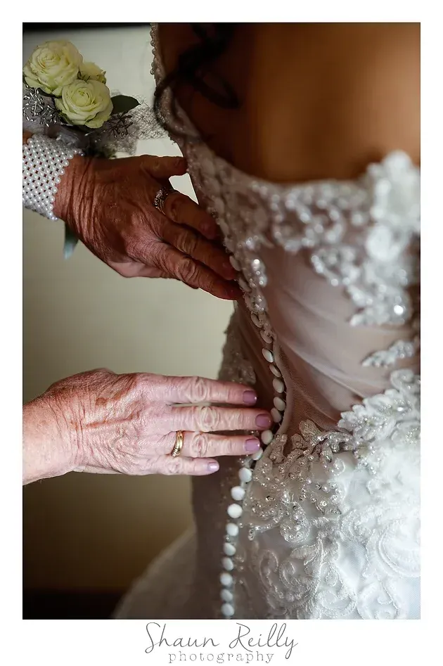 Hands fastening the back of a beaded white dress, close-up with lace and floral details