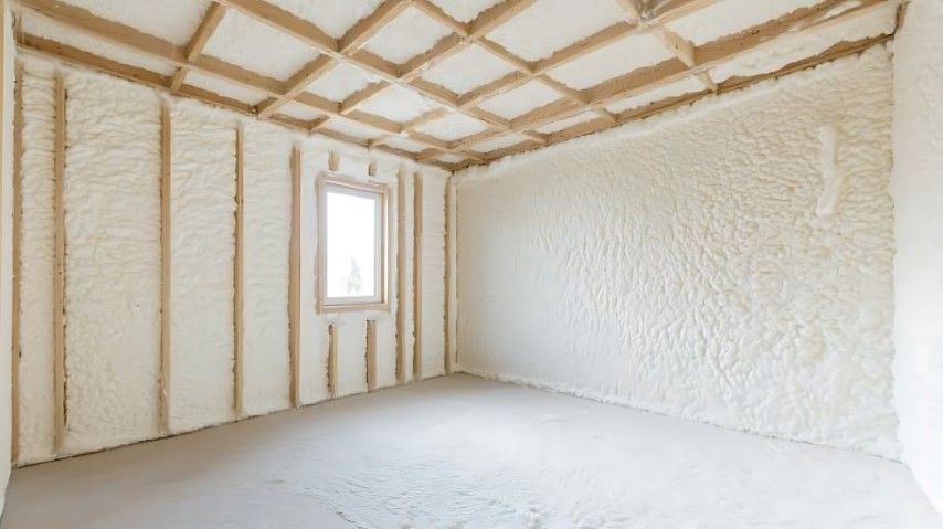 Empty white room with exposed insulation, sloped ceiling beams, and a small window.