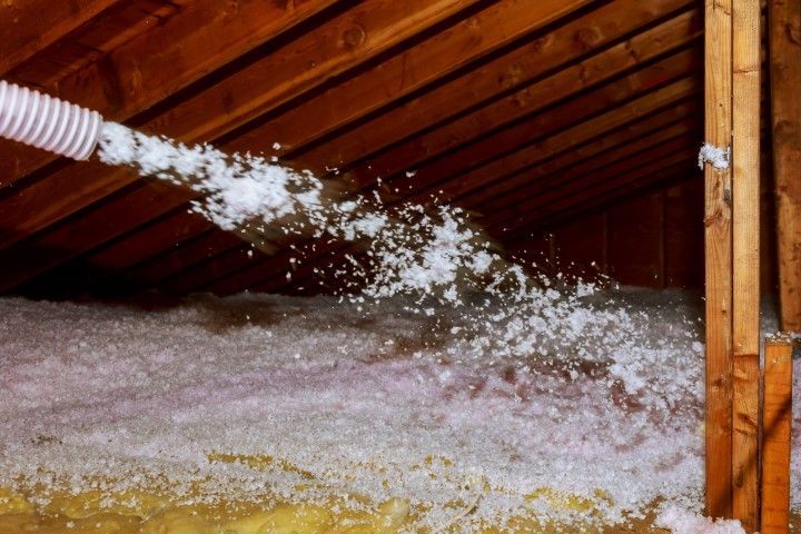 Insulated attic with blown-in white foam spraying from a hose onto the floor