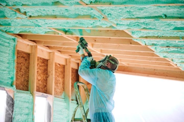 Worker spray-applying green insulation to a house ceiling during construction