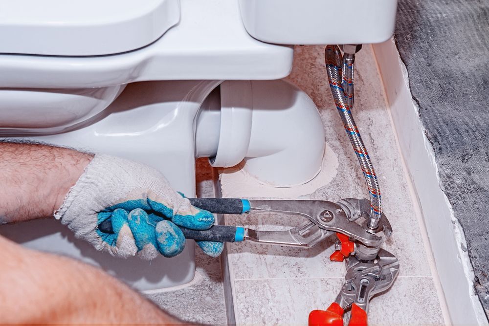 A Man is Fixing a Toilet With a Pair of Pliers — Approved Plumbing Service in Burrum Heads, QLD