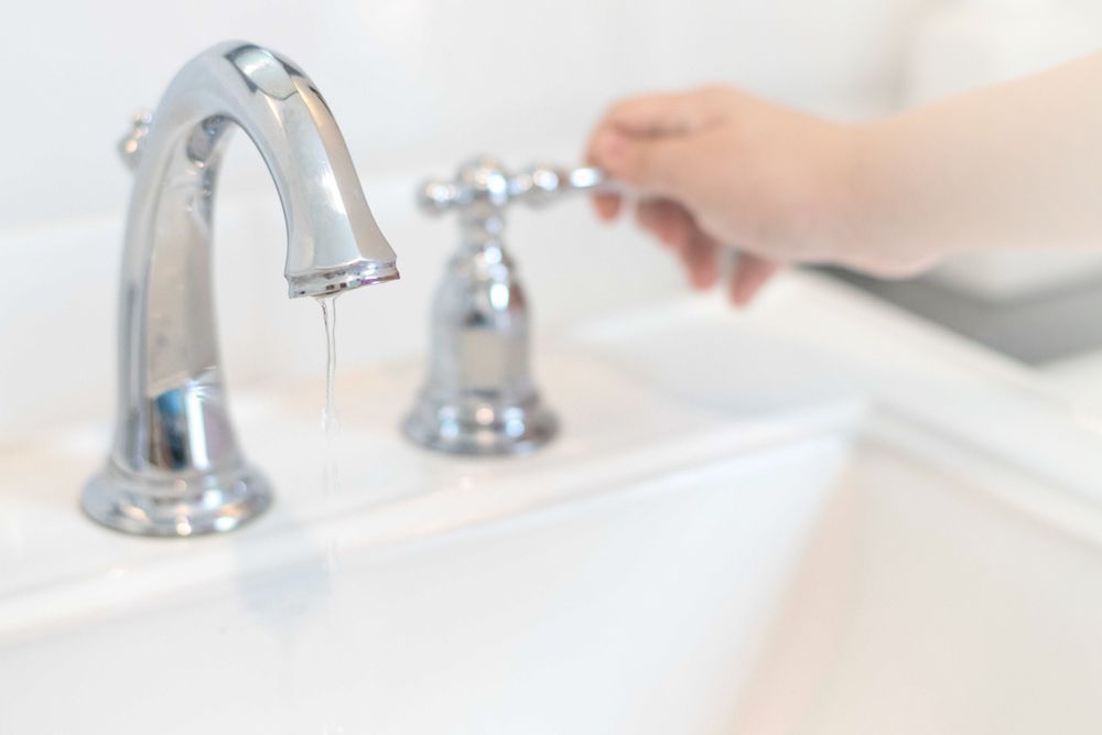 A Person is Turning on a Bathroom Sink Faucet — Approved Plumbing Service in Burrum Heads, QLD