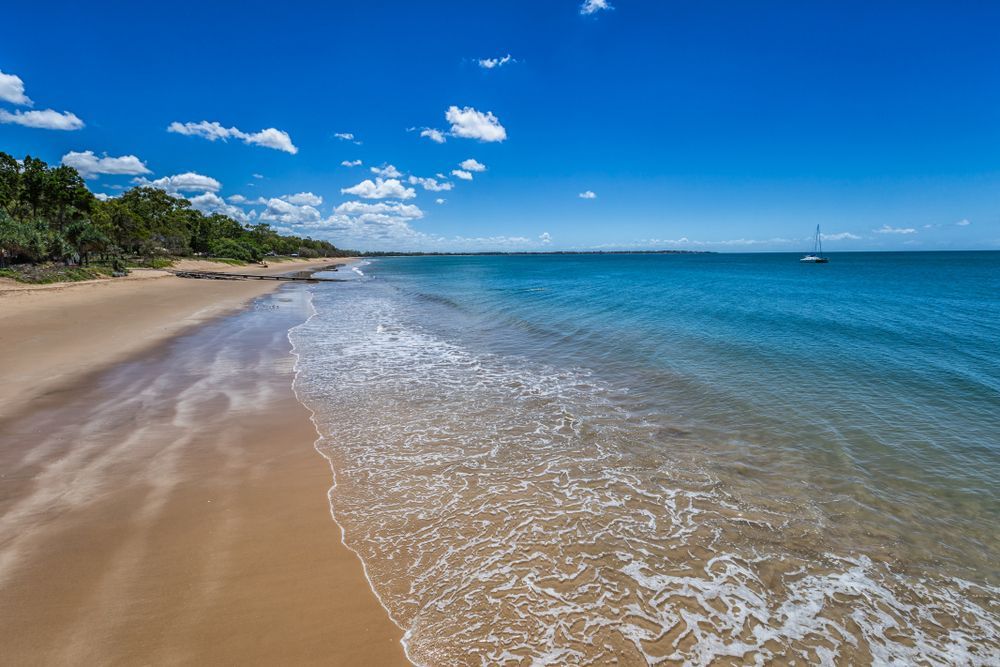 A Beach With Waves Crashing on the Sand and a Boat in the Distance — Approved Plumbing Service in Hervey Bay, QLD