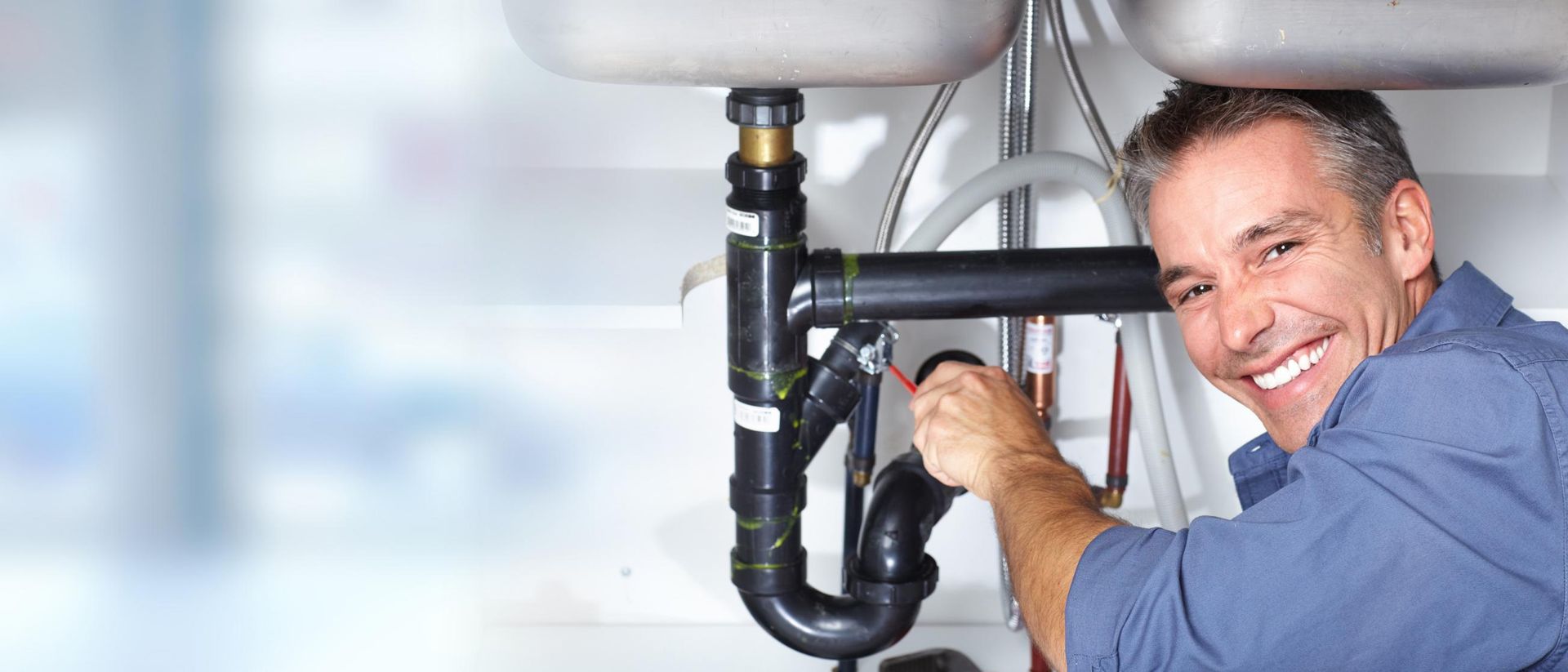 Man is Fixing a Sink With a Wrench and Smiling — Approved Plumbing Service in Darwin, NT