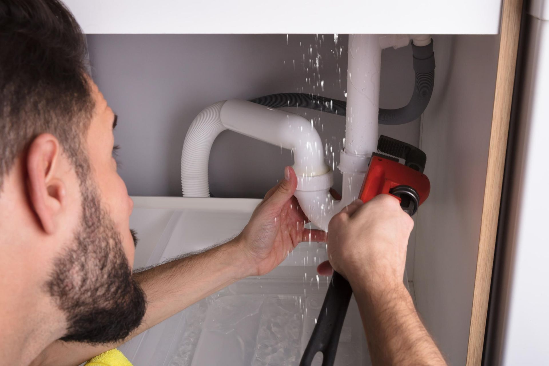 Man is Fixing a Leaking Sink Pipe With a Wrench — Approved Plumbing Service in Woolner, NT