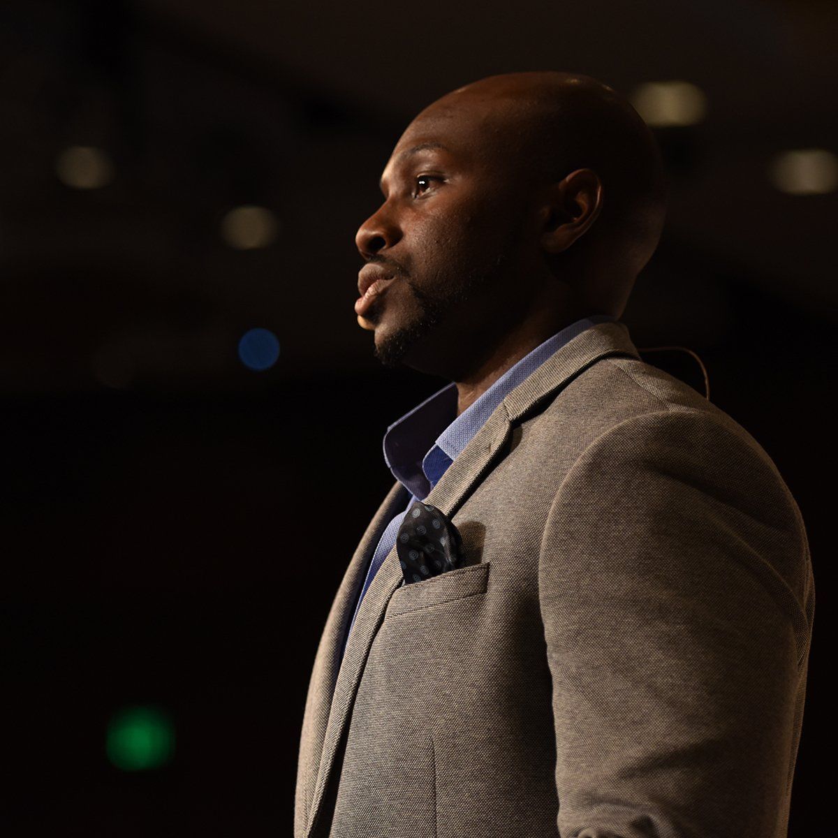 A Juntae Delanein, a suit, is standing in a dark room.