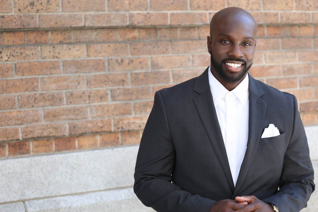 A Juntae Delane in a suit and tie is standing in front of a brick wall.