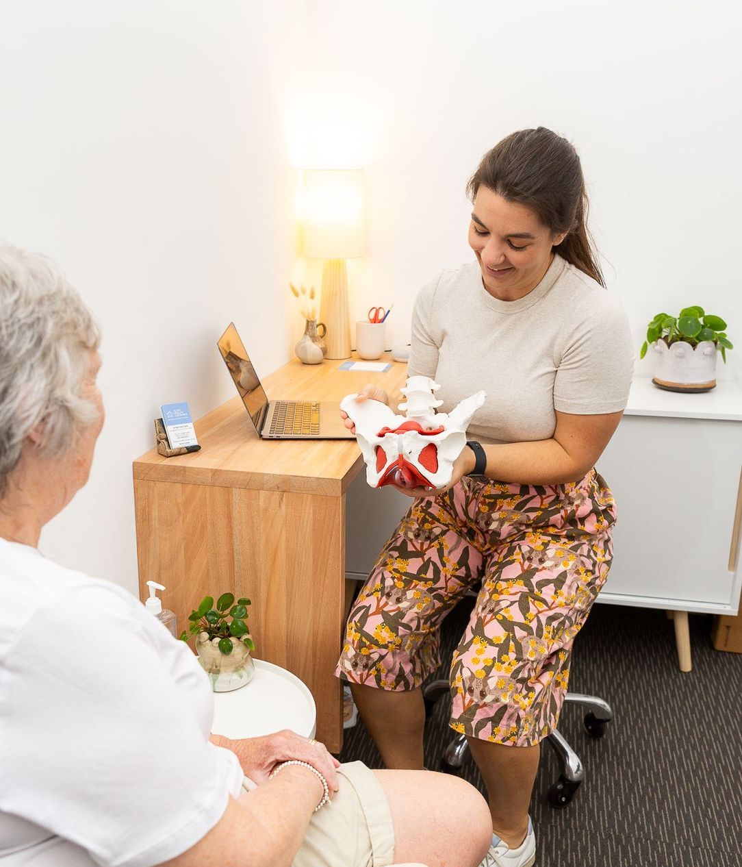 A woman is holding a model of the pelvis while talking to an older woman — Align Health Therapies in Woonona, NSW