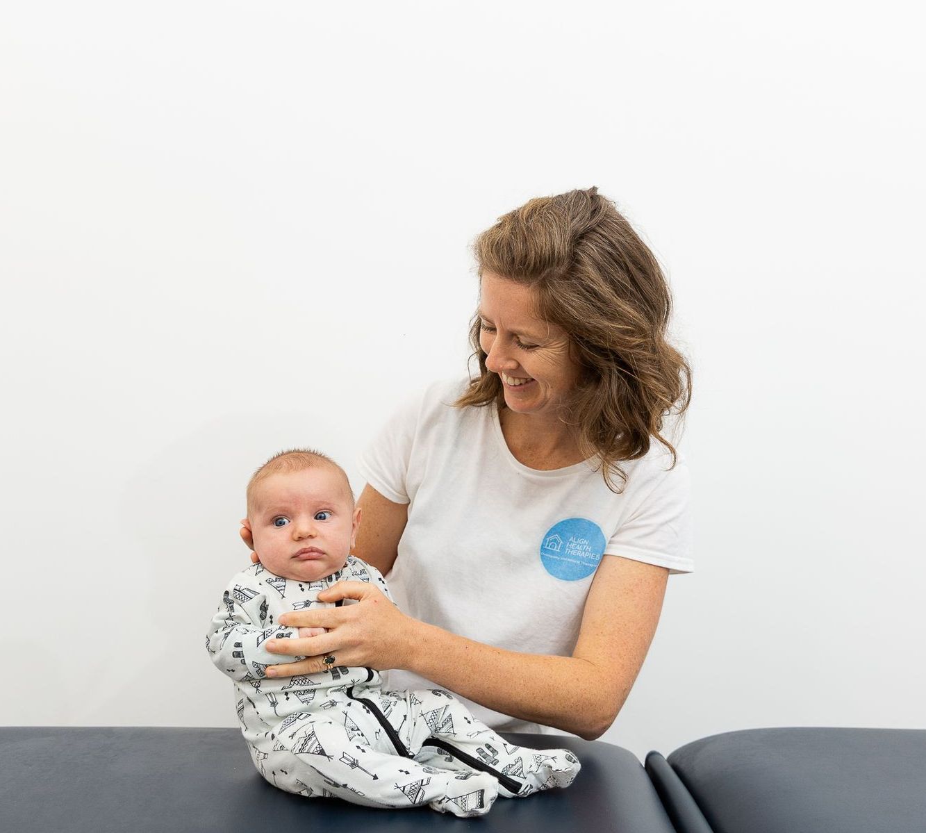 A woman is holding a baby on a table — Align Health Therapies in Woonona, NSW