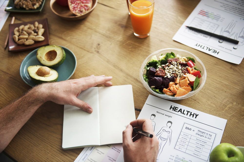 A Man Is Writing in A Notebook Next to A Bowl of Salad — Align Health Therapies in Woonona, NSW