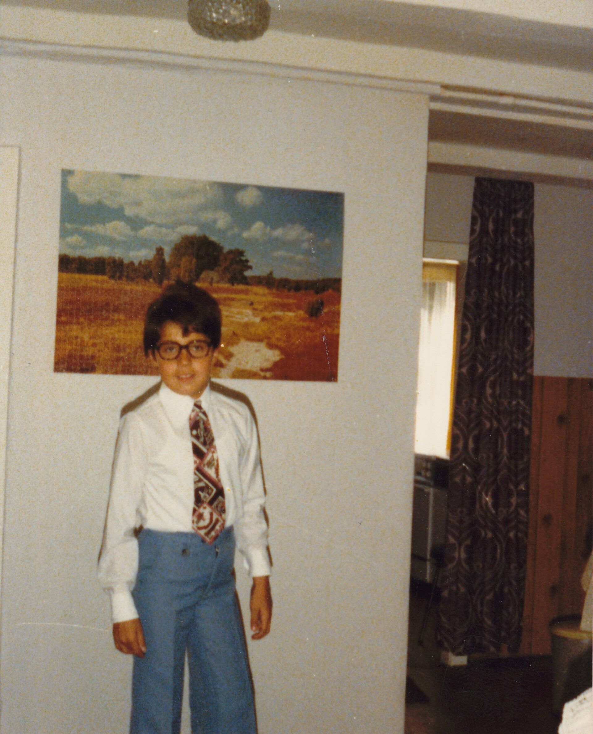 Marcus Fleischer als Junge Mitte der 1970er-Jahre mit brauner Hornbrille, blauer Schlaghose, weißem Hemd und gemusterter Krawatte vor einem Landschaftspuzzle