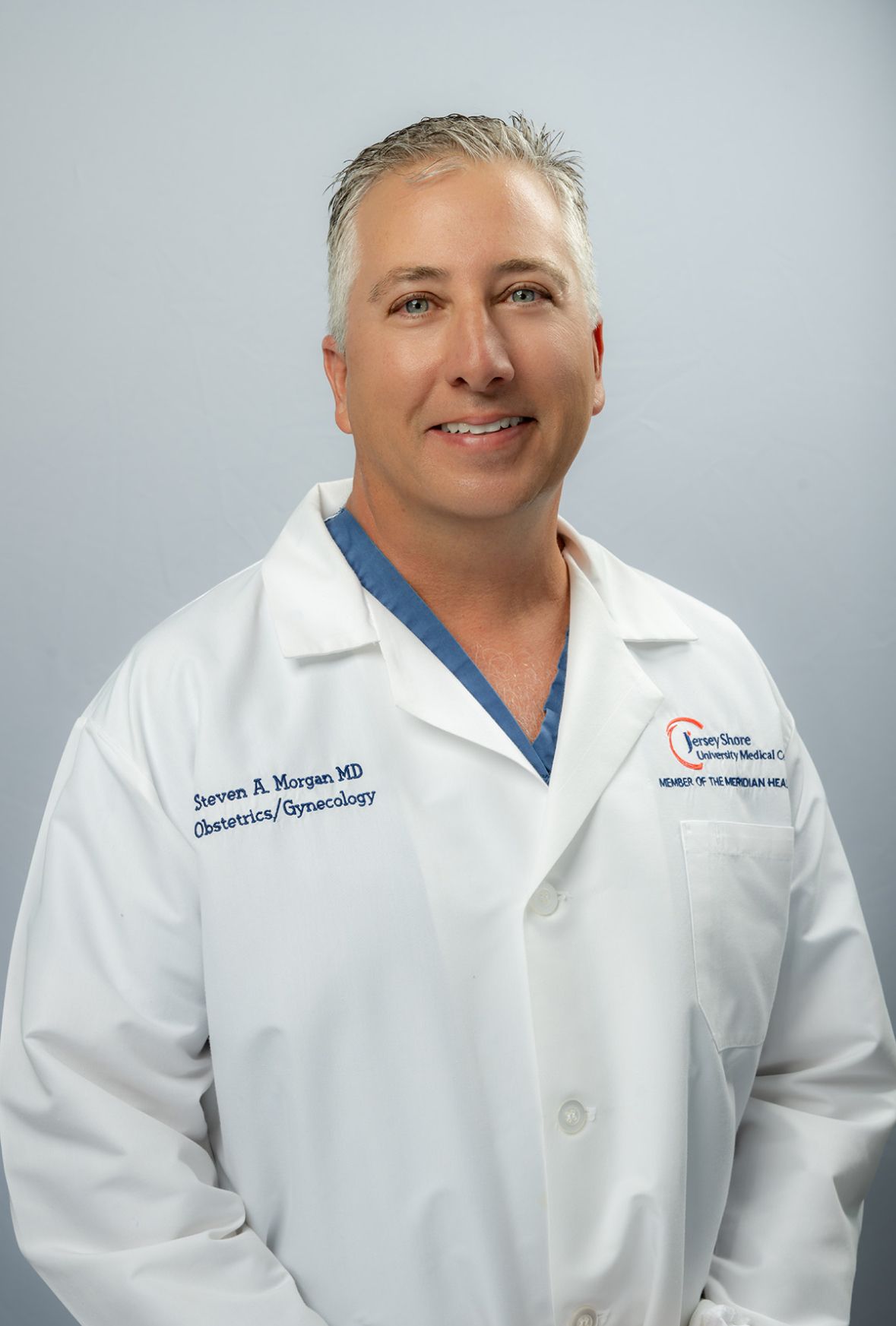 Doctor in a white lab coat smiling against a light gray background