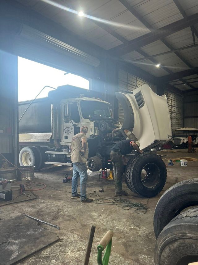 Mechanic working on a large white dump truck inside a repair shop with other truck parts nearby | Sellers Wrecker & Repair