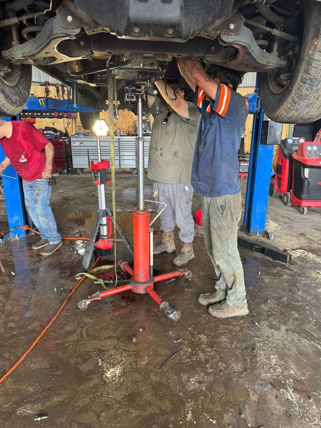 Mechanics working under a raised car in an auto repair shop with a hydraulic lift and tools nearby | Sellers Wrecker & Repair