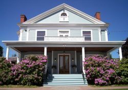 Light blue Victorian house with porch, shrubs, and blue steps.