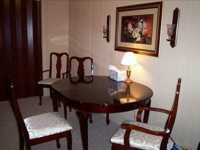 Dining room: oval table, four chairs, floral painting, lamp, and sconces.