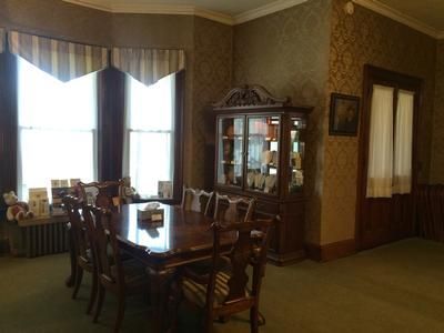 Dining room with a table, chairs, display cabinet, and window. Green carpet, patterned wallpaper.