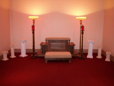 Red-carpeted room with tan bench and side tables, flanked by lamps and decorative white pillars. Warm lighting.