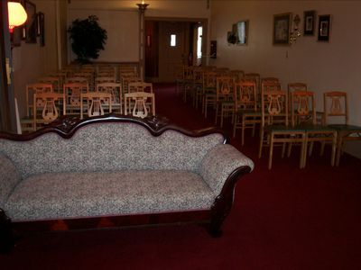Interior of a room with a patterned sofa, rows of chairs, and red carpet.