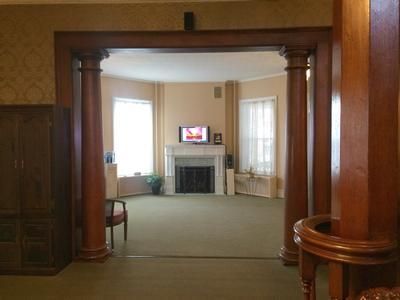Room with wooden pillars, fireplace, and TV. Green carpet, tan walls, and a built-in cabinet.