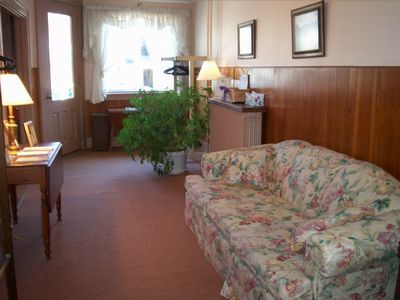 Waiting room with floral couch, wood paneling, and potted plant by window.