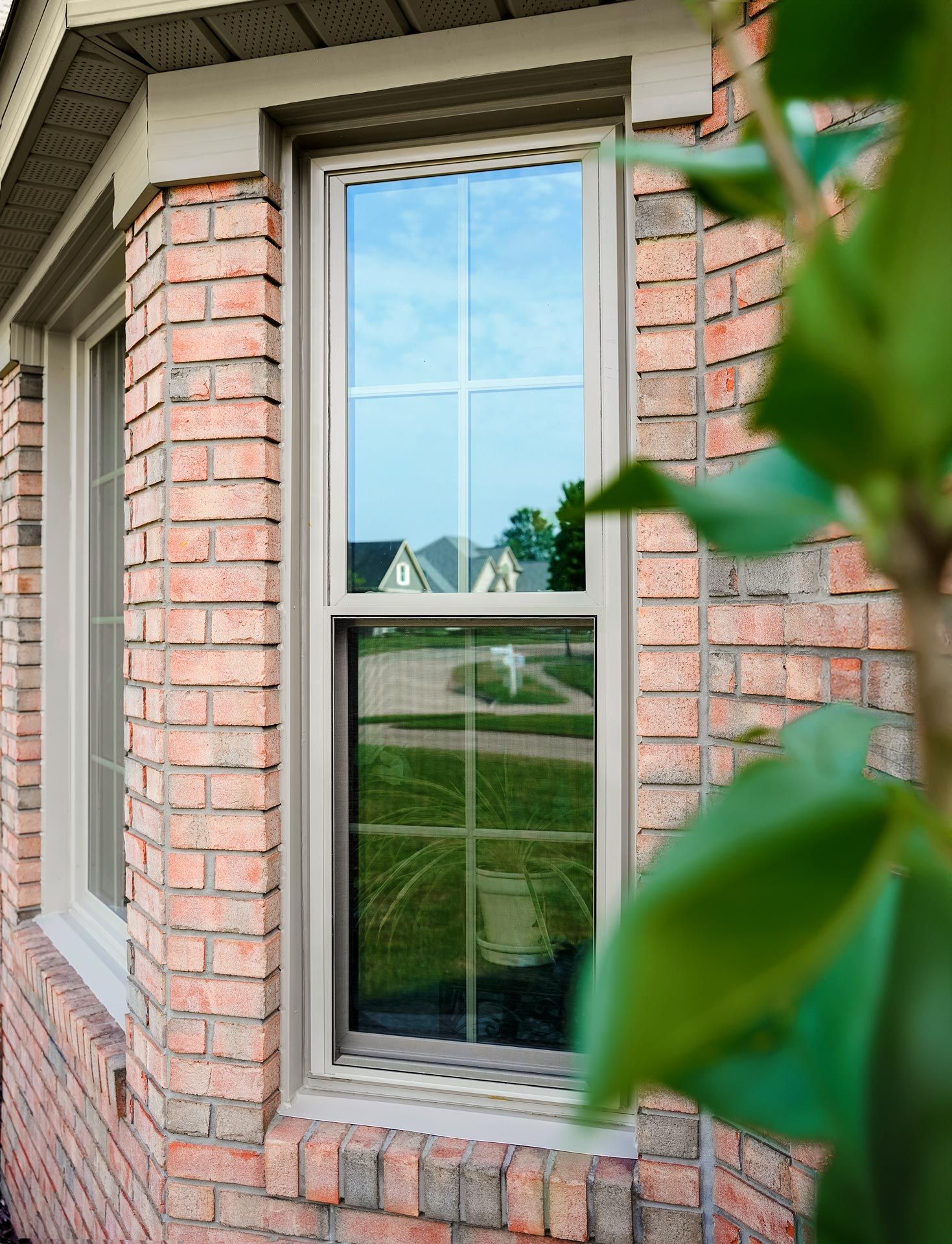 Tall, rectangular window in a red brick wall, reflecting a suburban street scene with trees and houses; the window frame is tan.