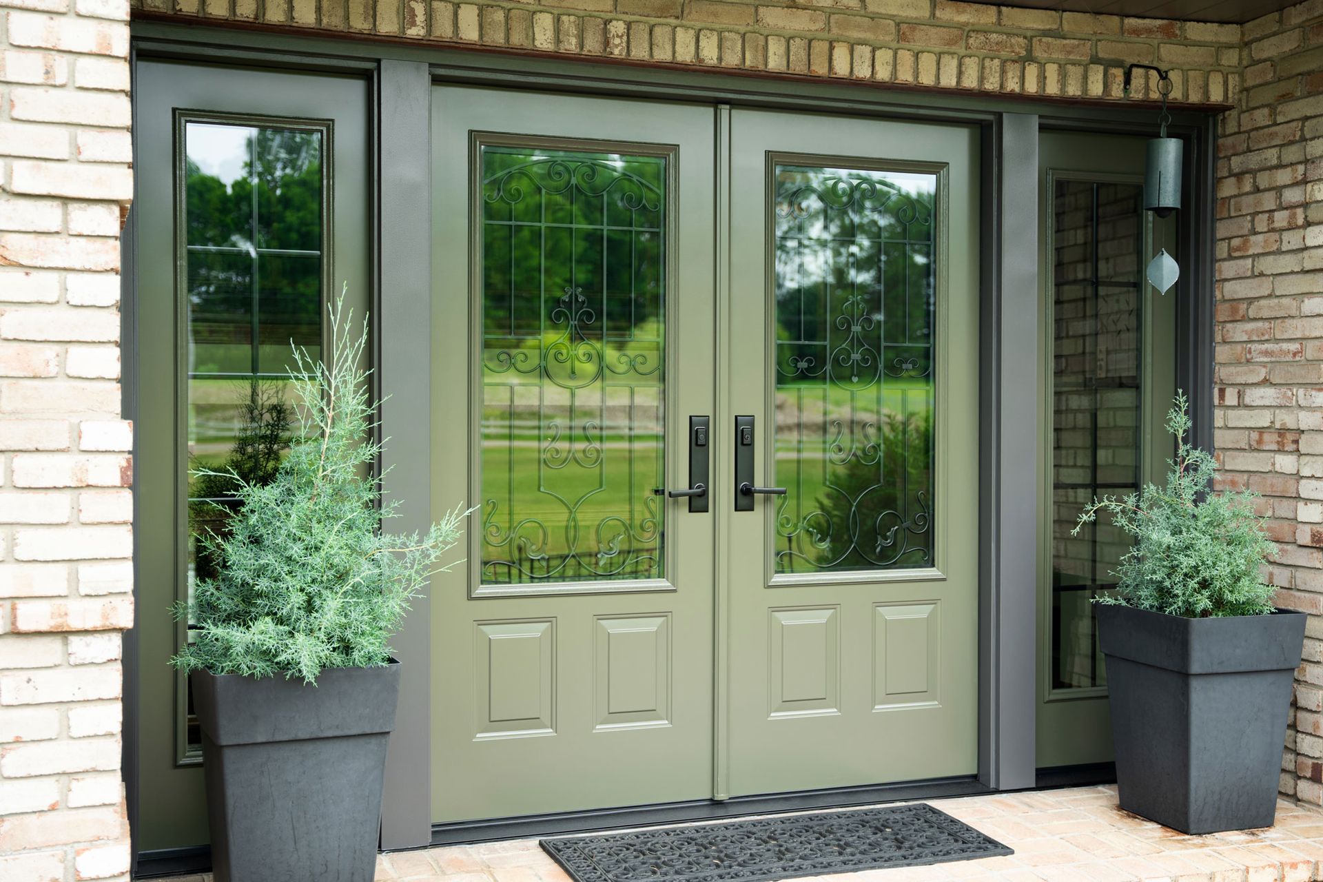 Double green front doors with glass panels flanked by brick and two potted plants.