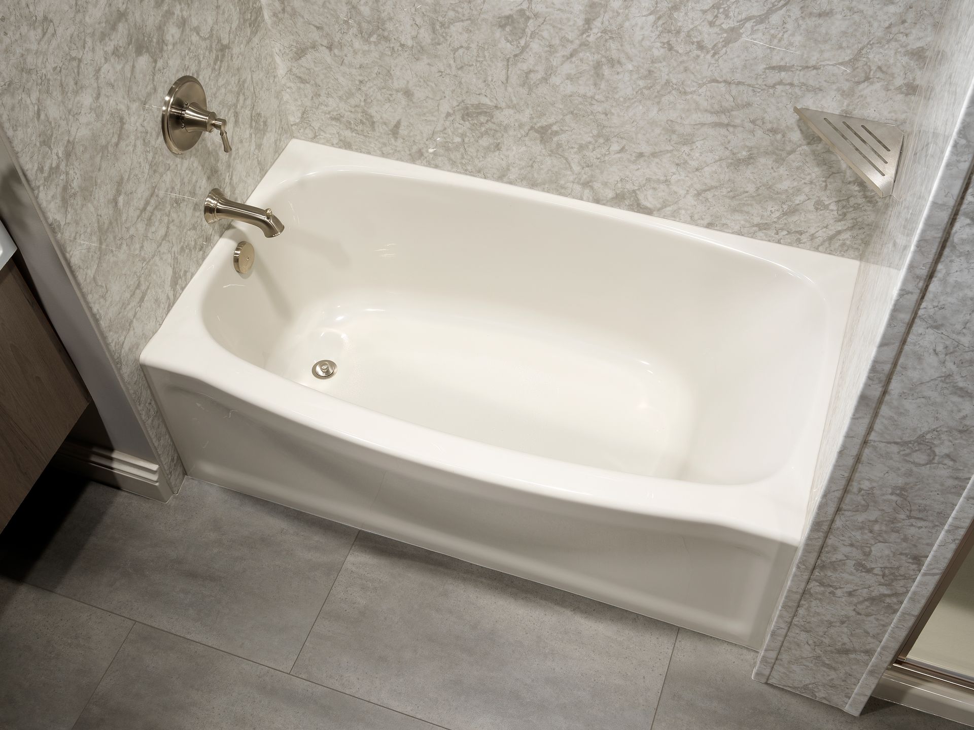 White bathtub in a modern bathroom, with silver fixtures and gray tile walls and floor.
