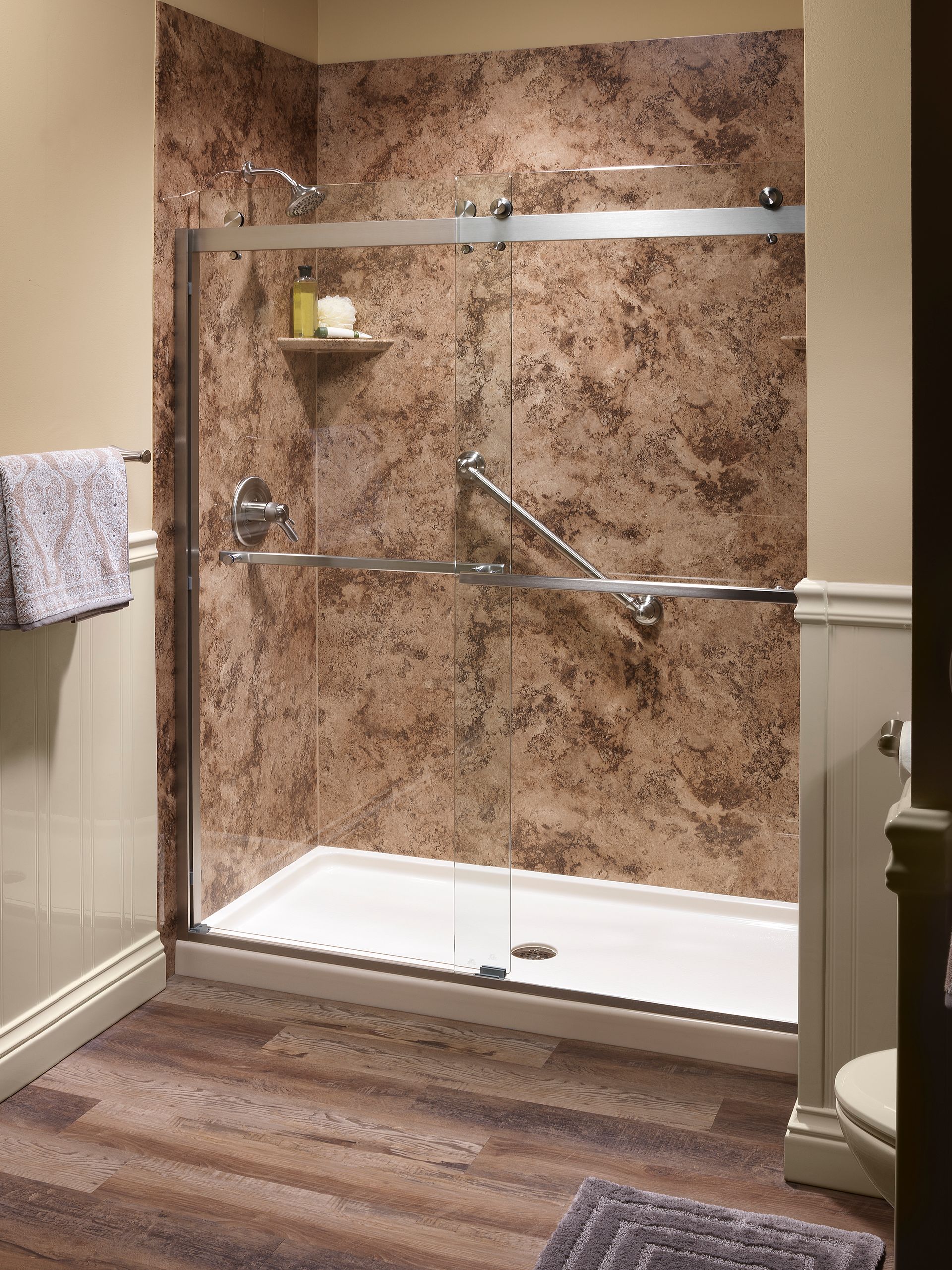 Shower with brown marbled walls, grab bar, and sliding glass doors in a bathroom.