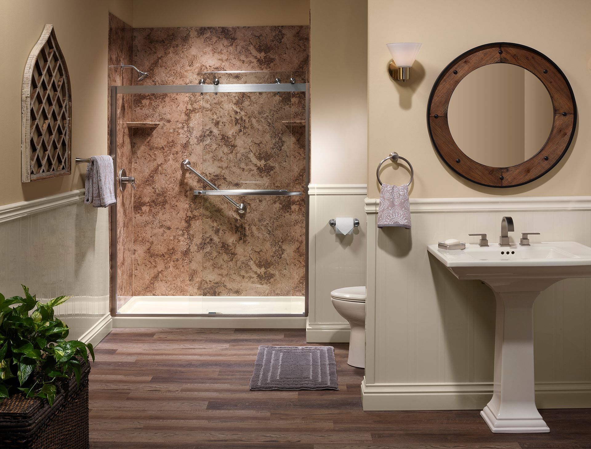 Bathroom with shower and pedestal sink; brown marble shower, wood-look floor, round mirror.