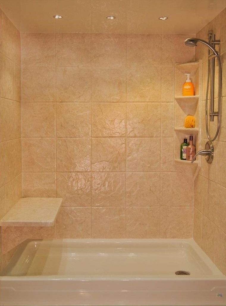 Bathroom shower with beige tiled walls, white tub, built-in shelves, and a shower seat.