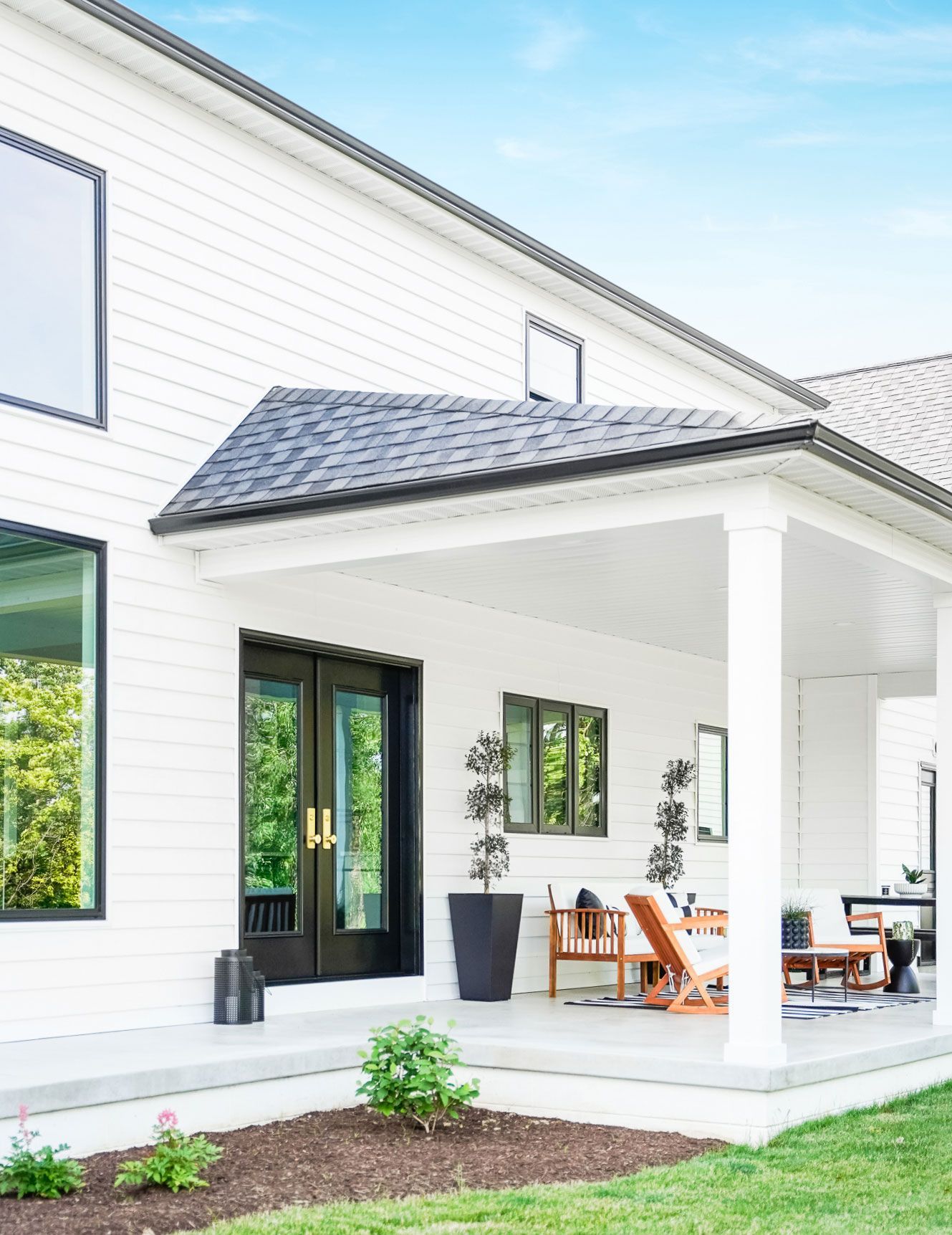 White house with black trim and a covered porch with seating.