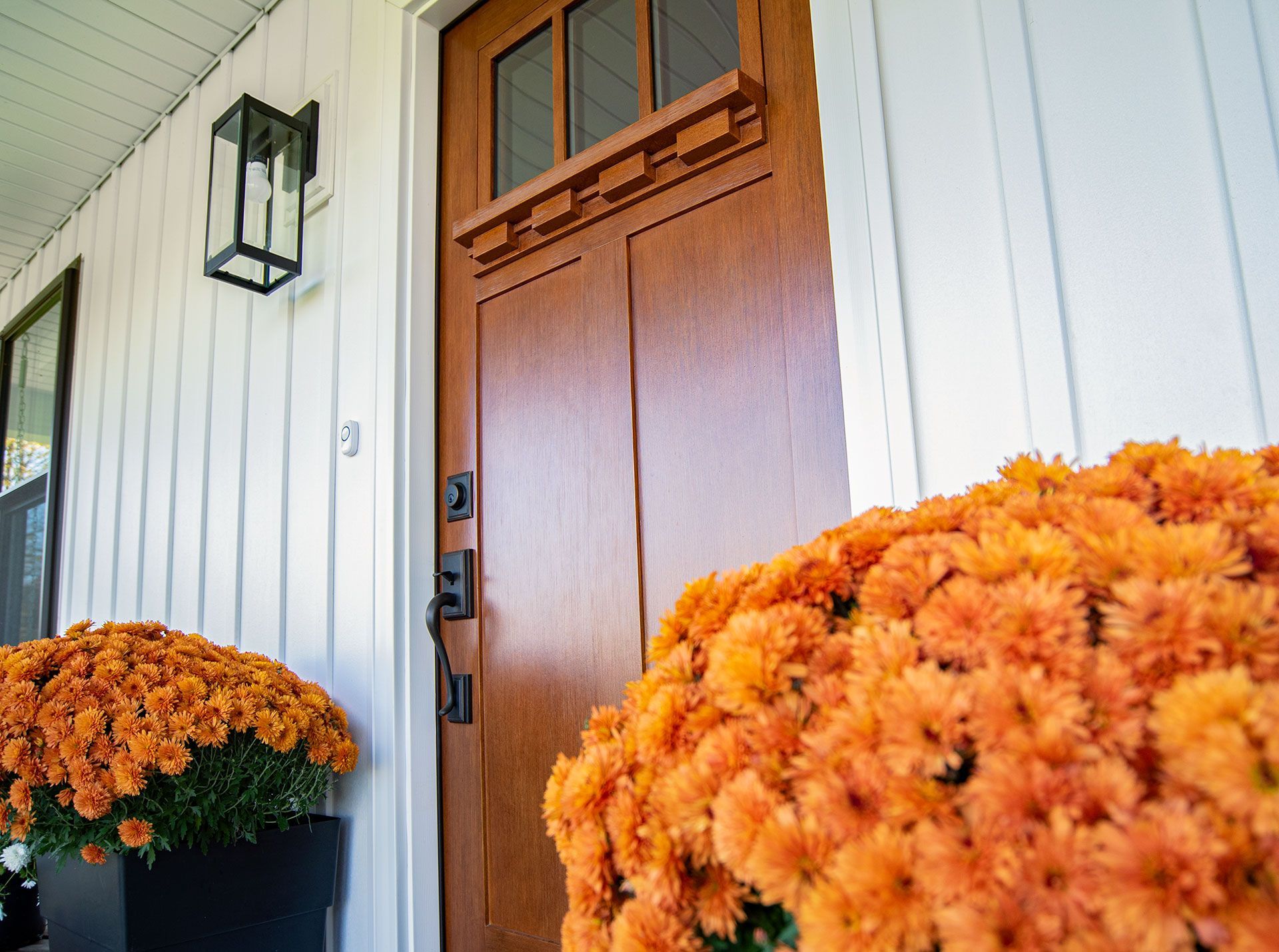 Brown front door with orange mums, black lantern, and white siding.