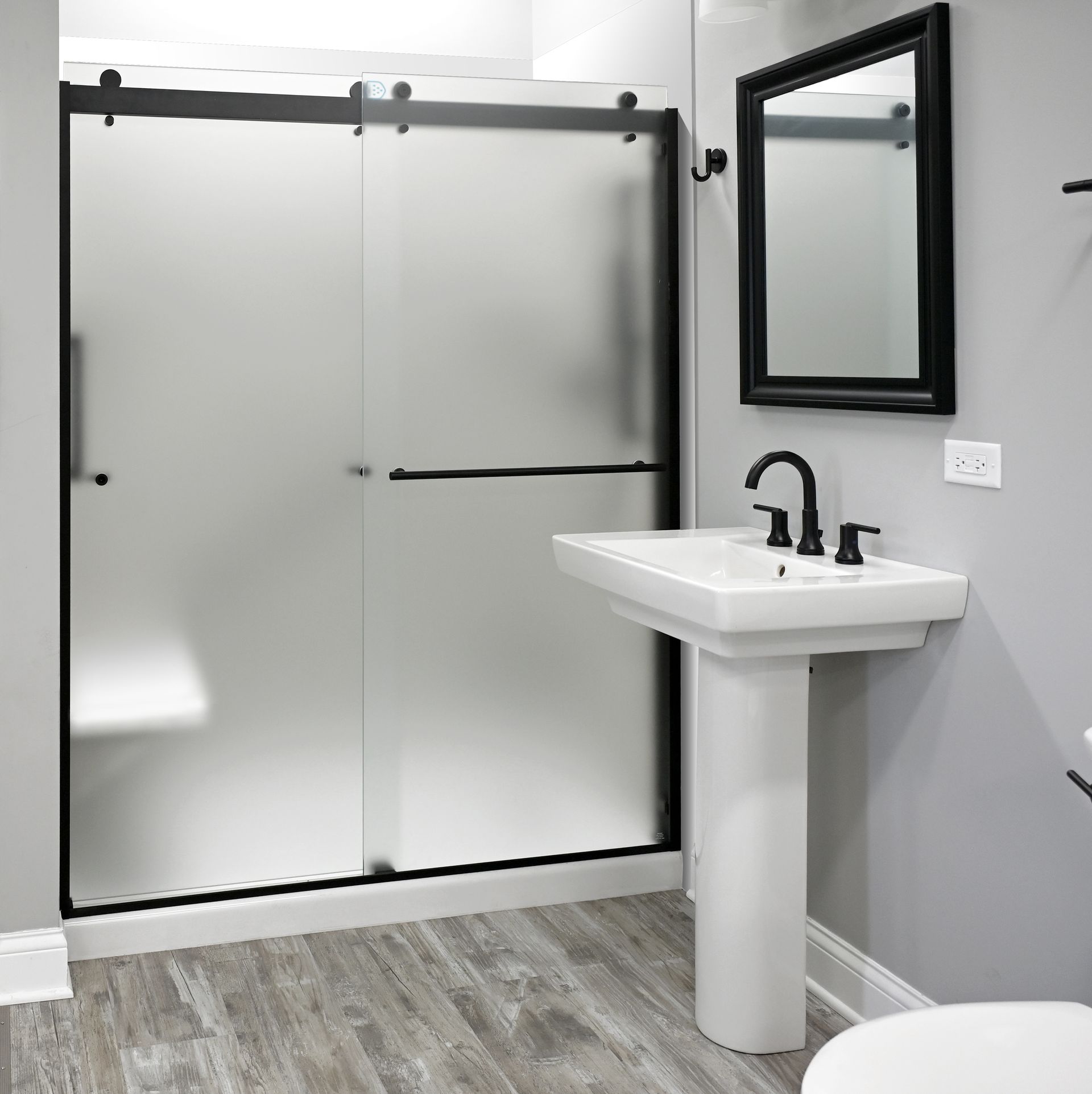 Bathroom with gray walls, frosted glass shower, pedestal sink, and black fixtures.