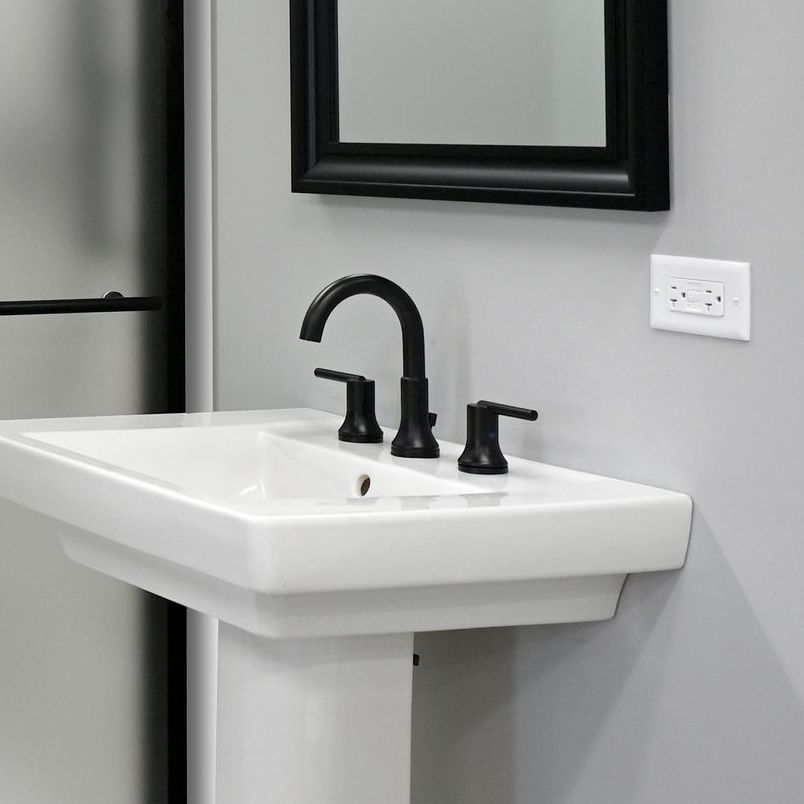 White pedestal sink with black faucet against gray wall, black-framed mirror.