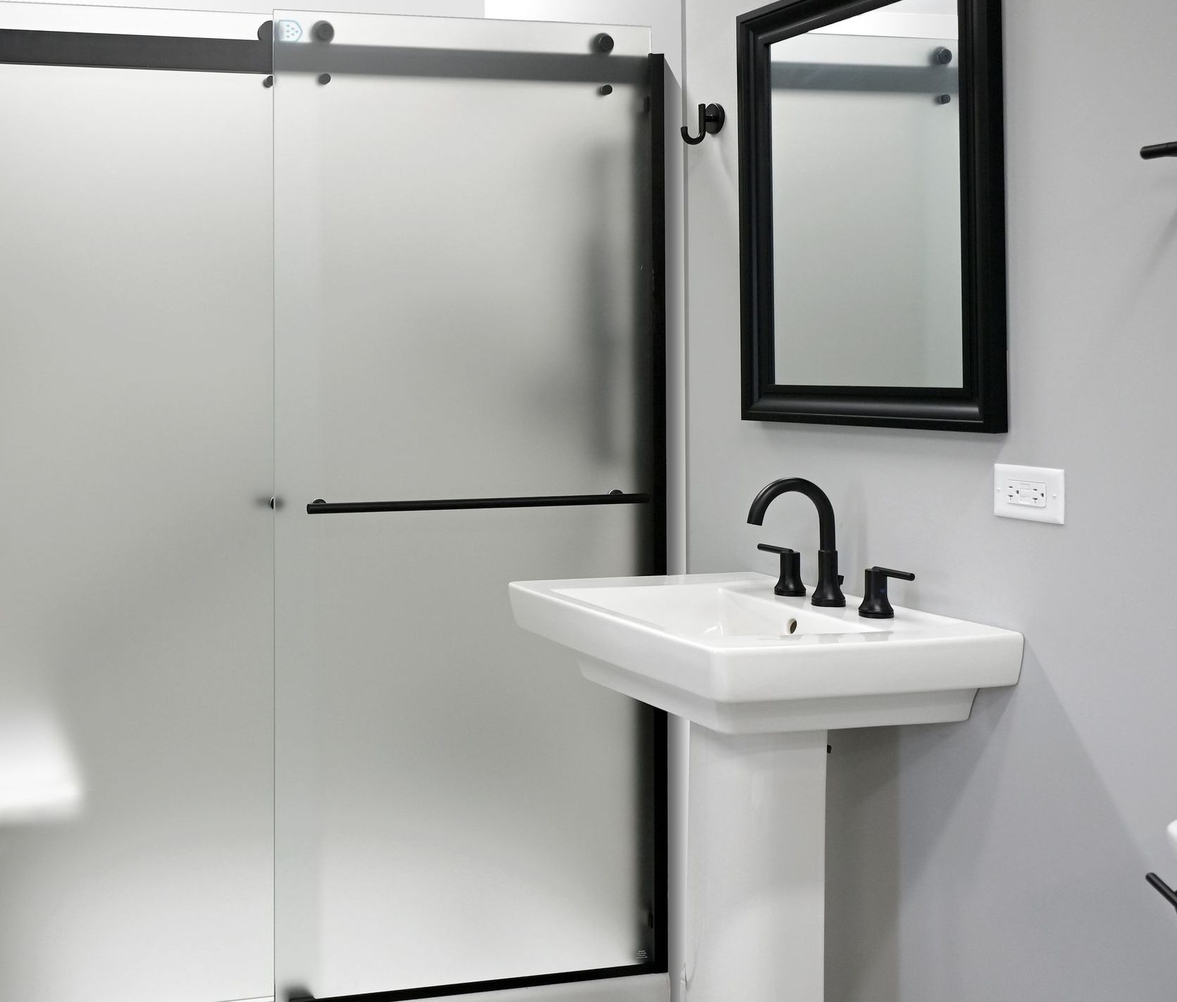 Bathroom with frosted glass shower doors, pedestal sink, black faucet and mirror.