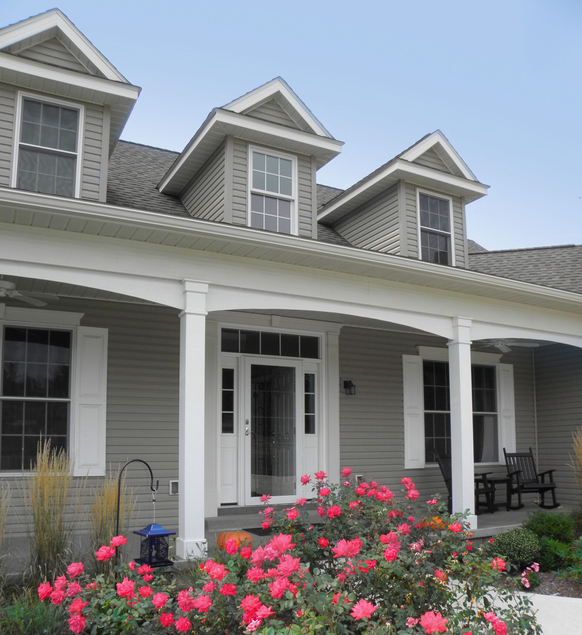 House with a porch and dormer windows, surrounded by a garden of pink roses.