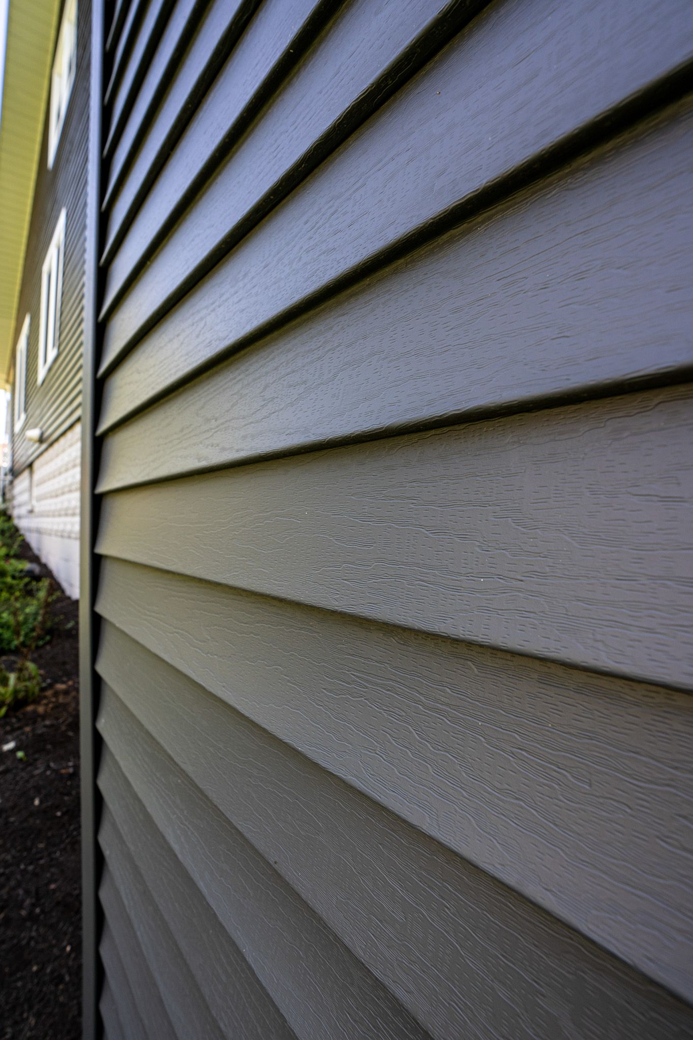 Gray, textured vinyl siding on a building's exterior, viewed at an angle.