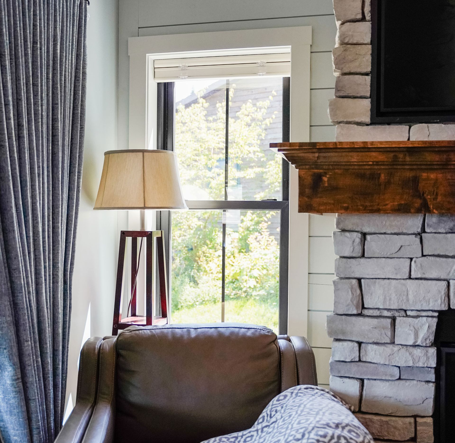 Cozy living room with stone fireplace, armchair, lamp, and window with greenery.
