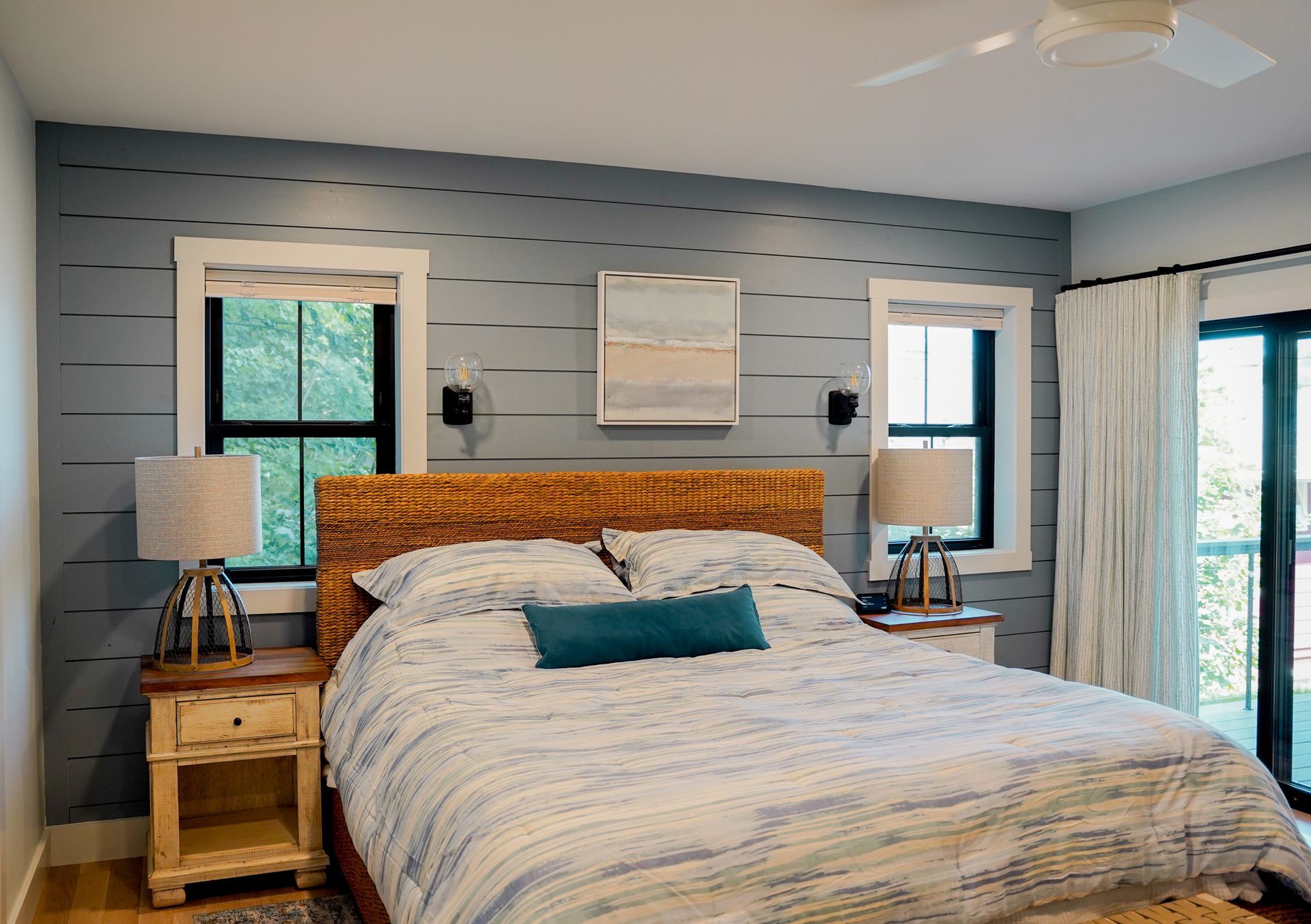 Bedroom with blue shiplap accent wall, two windows, woven headboard, and bedside tables with lamps.