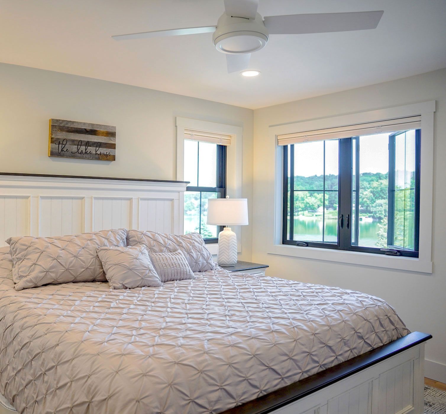 Bedroom with a king-sized bed, white furniture, and large windows overlooking a lake.