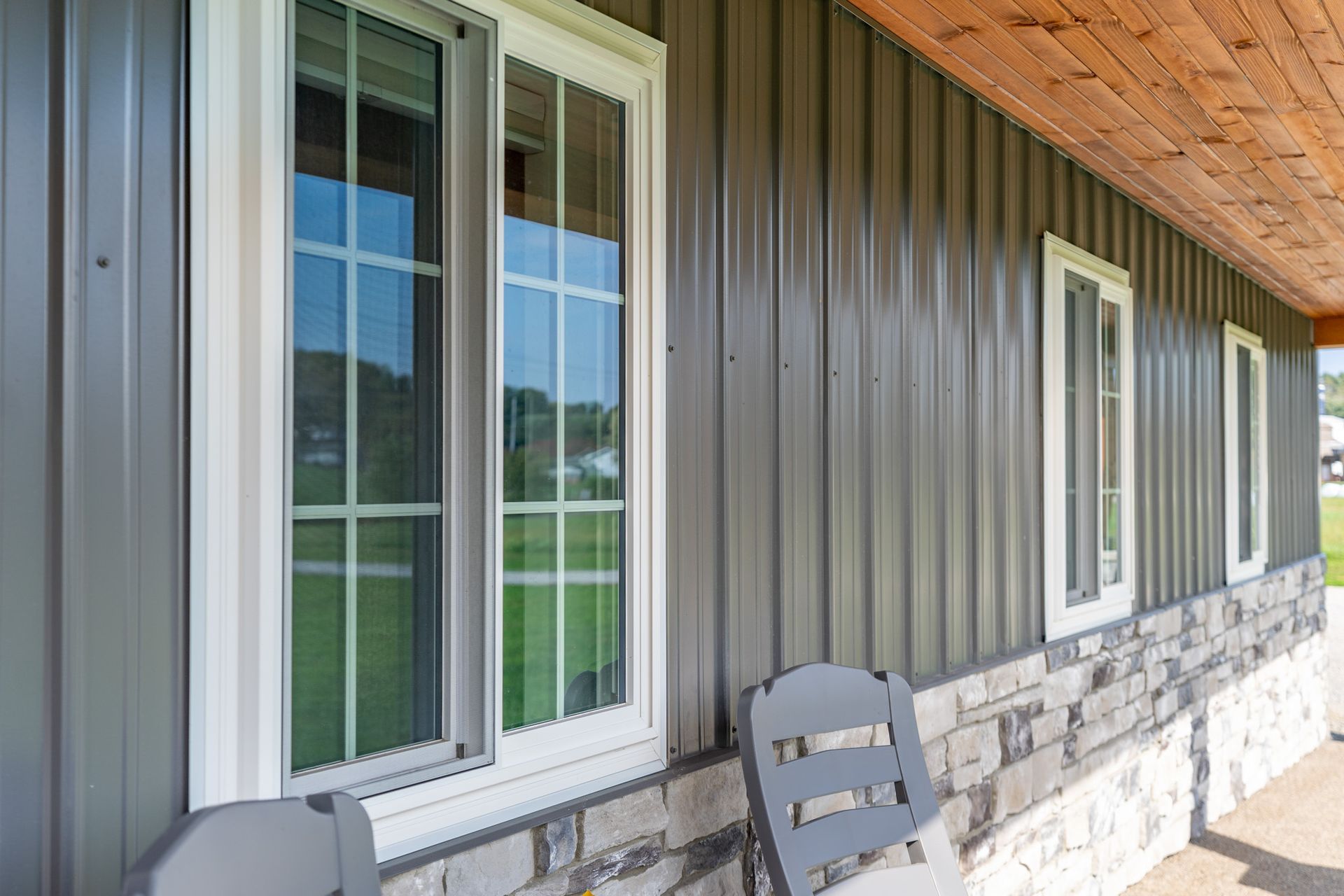 Gray metal building exterior with white-framed windows, stone base, and wooden ceiling.