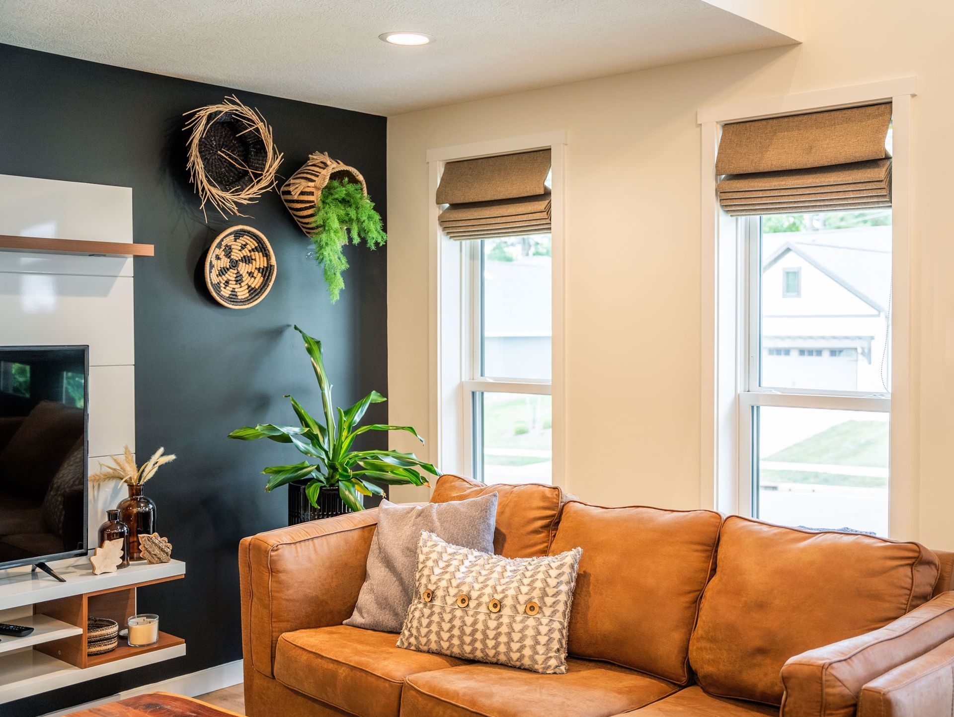 Living room with leather sofa, dark accent wall, woven baskets, and natural light from windows.