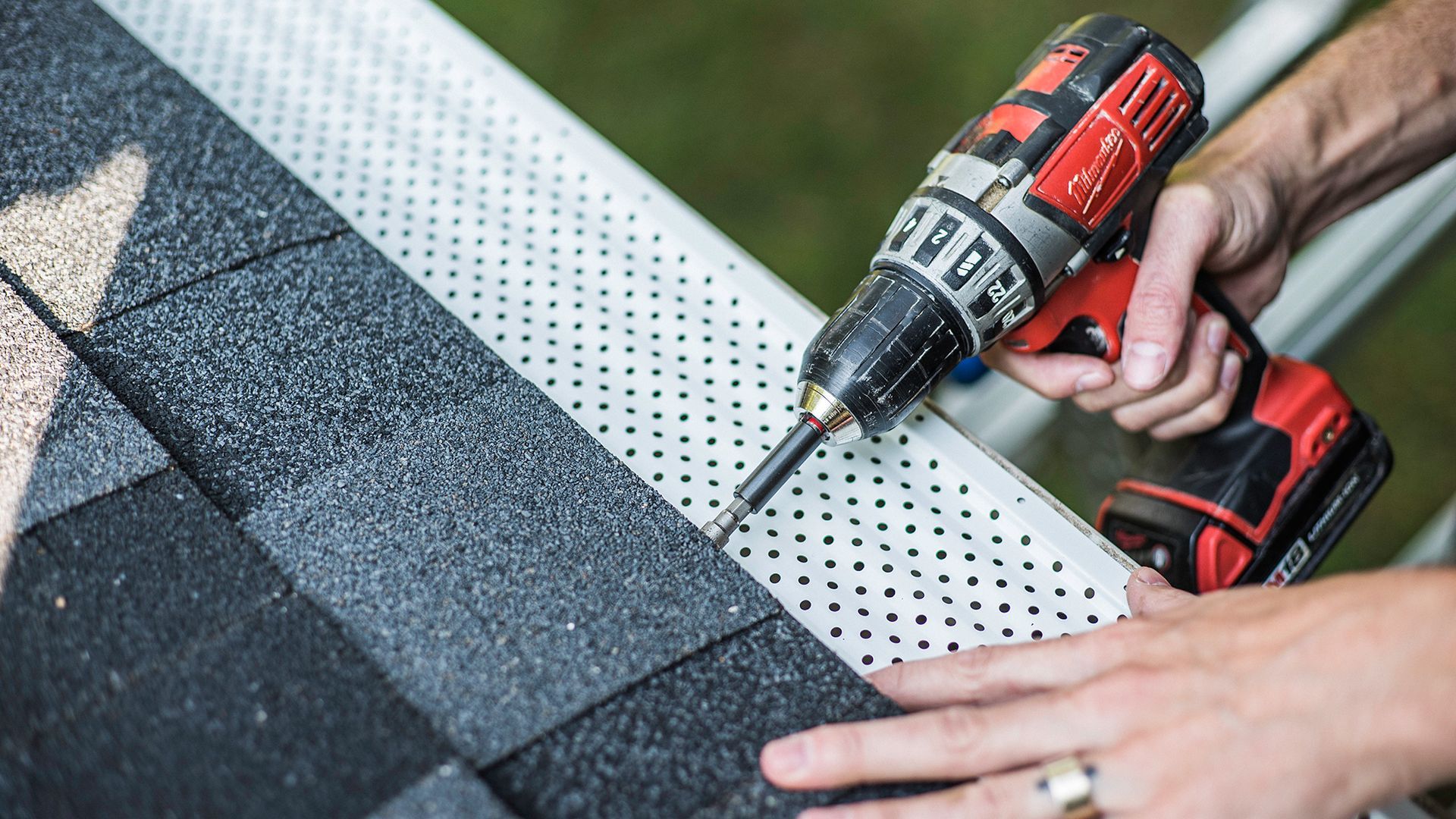 Person using a power drill to install a gutter guard on a roof.