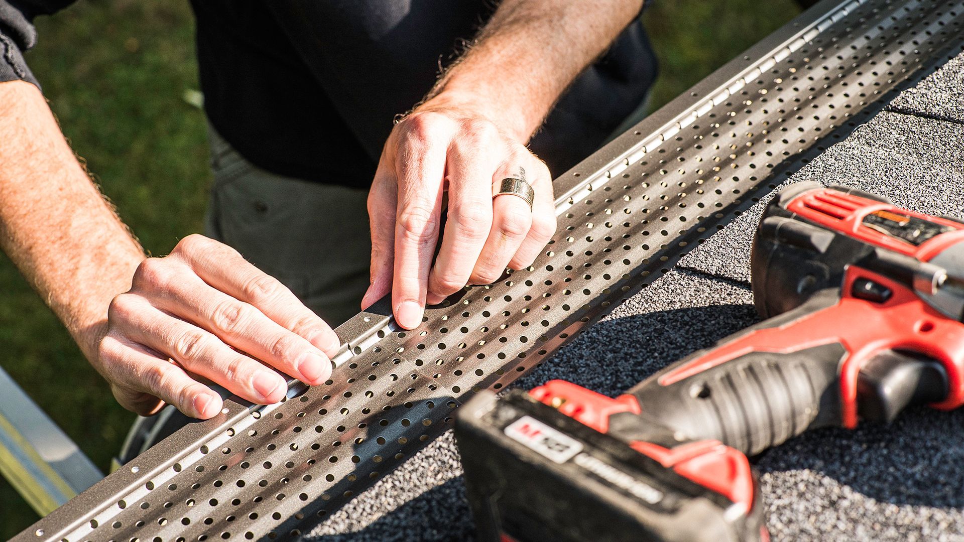 Person installing a gutter guard on a roof, using a drill.