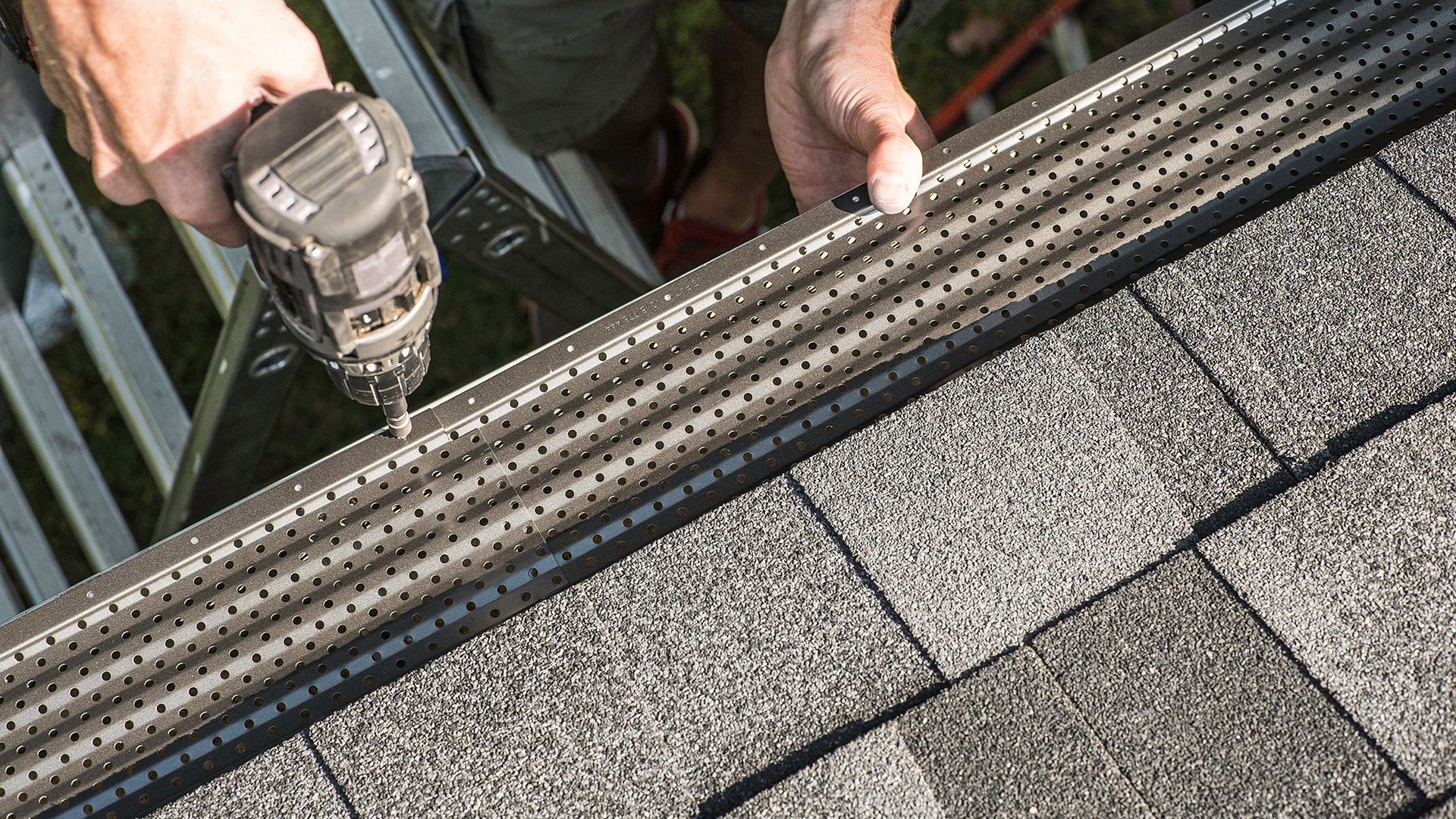 Person using a drill to install a gutter guard onto a roof.