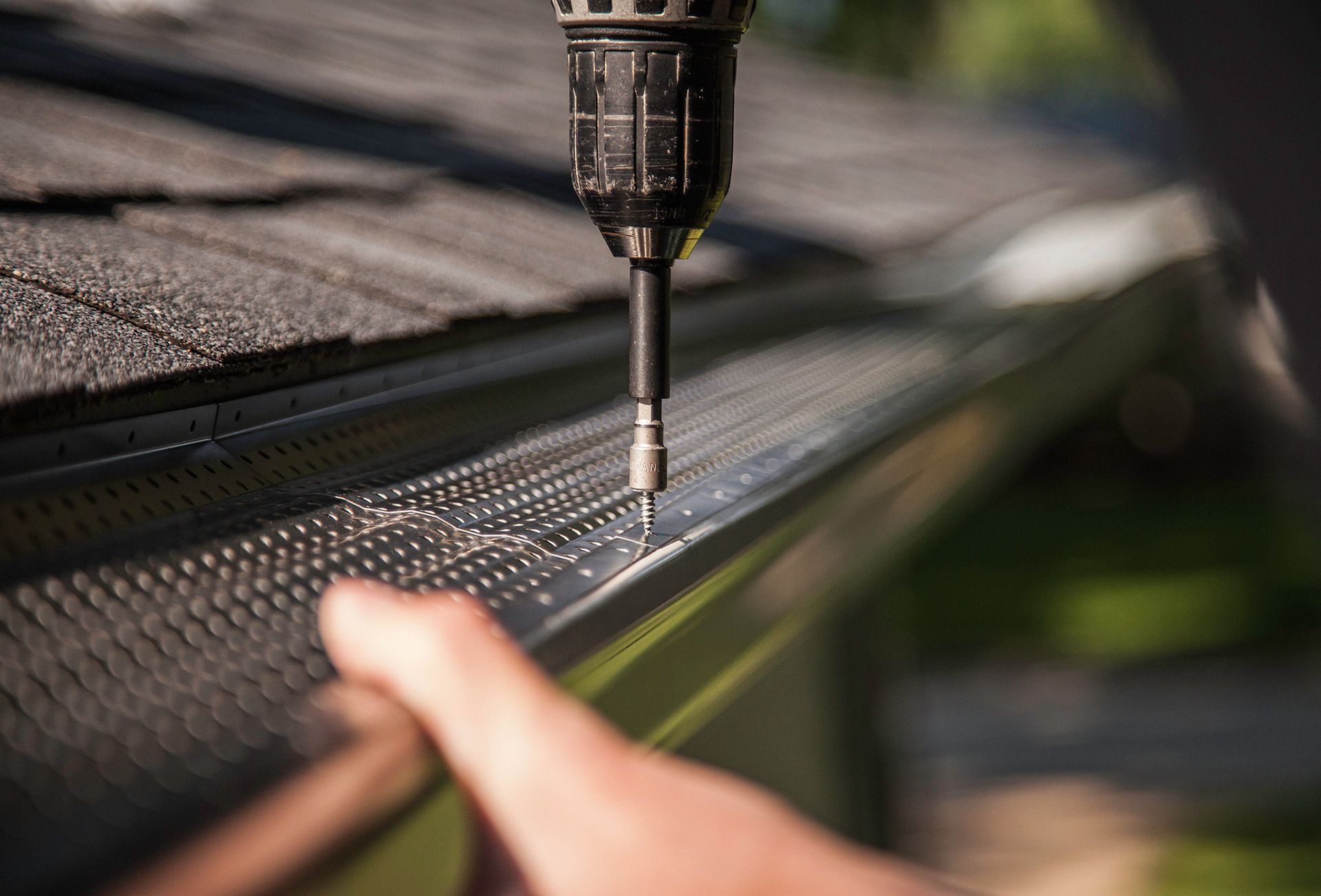 A person using a drill to install a gutter guard on a roof.