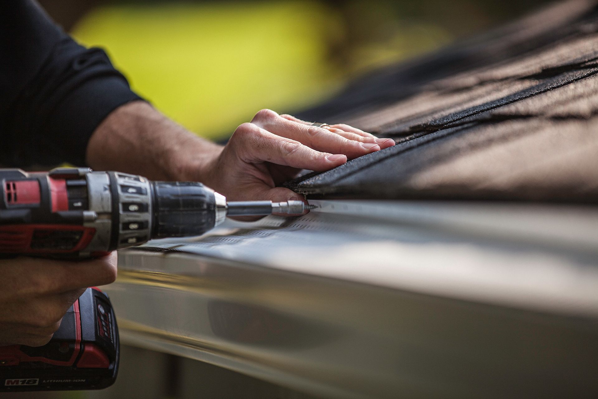 Person using a drill to install a gutter along the edge of a roof.