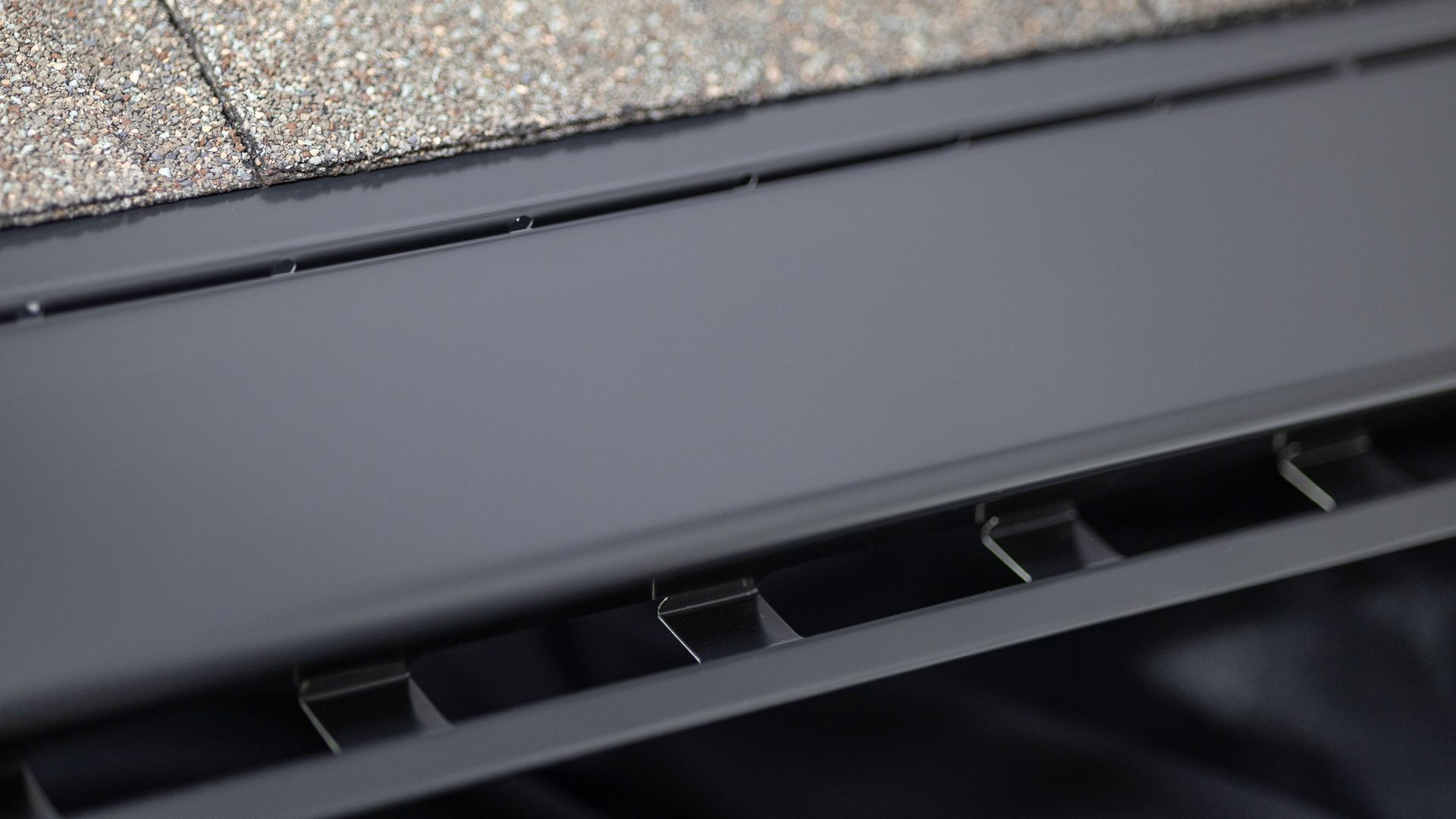 Dark gray gutter with debris guard installed along roof shingles.