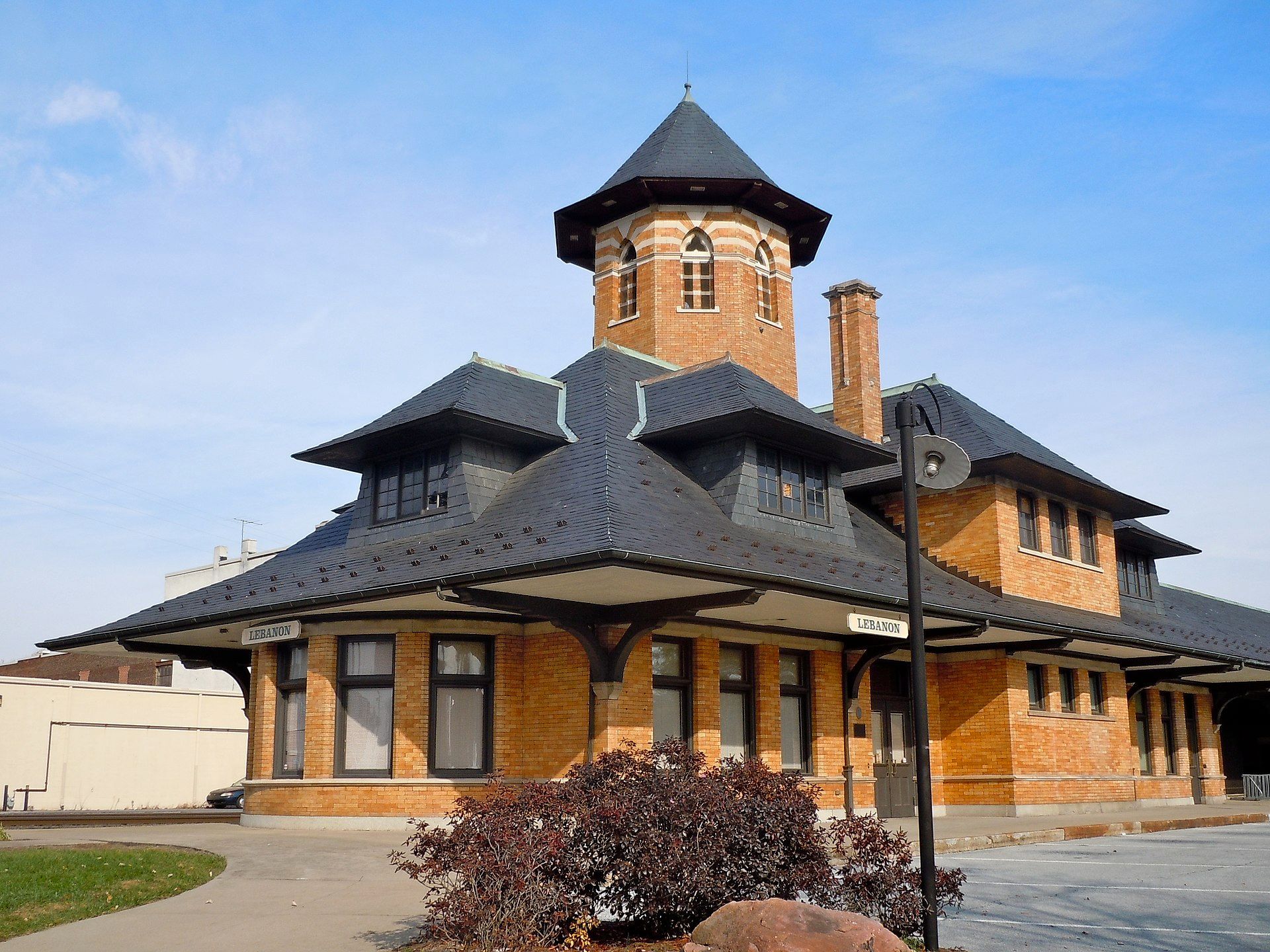Brick train depot with black roof and tower, under a blue sky.